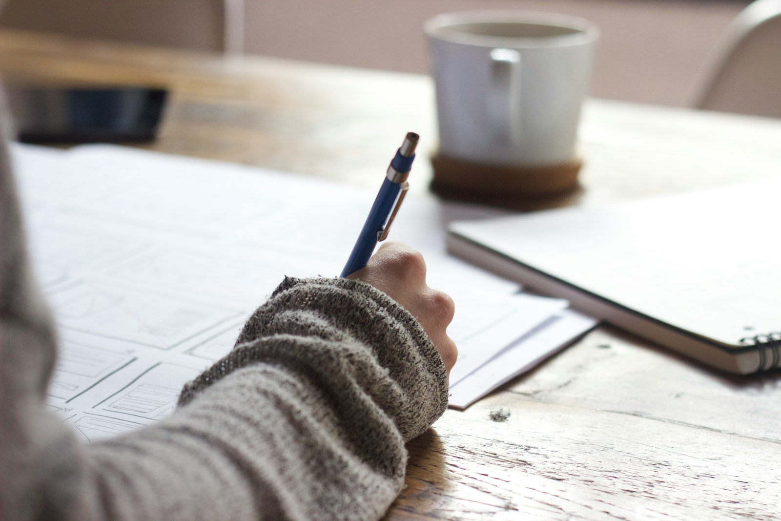 person signing personal liability coverage for homeowners on brown wooden table near white ceramic mug